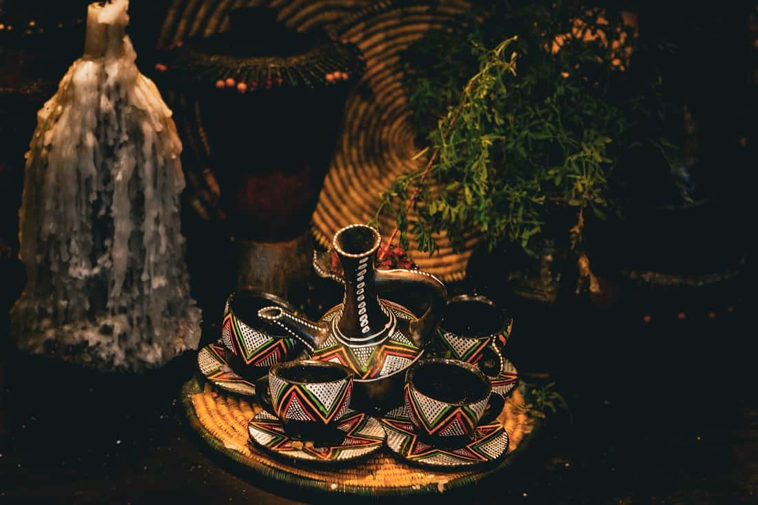 A jebena and painted finjal cups set out on a woven tray for a coffee ceremony
